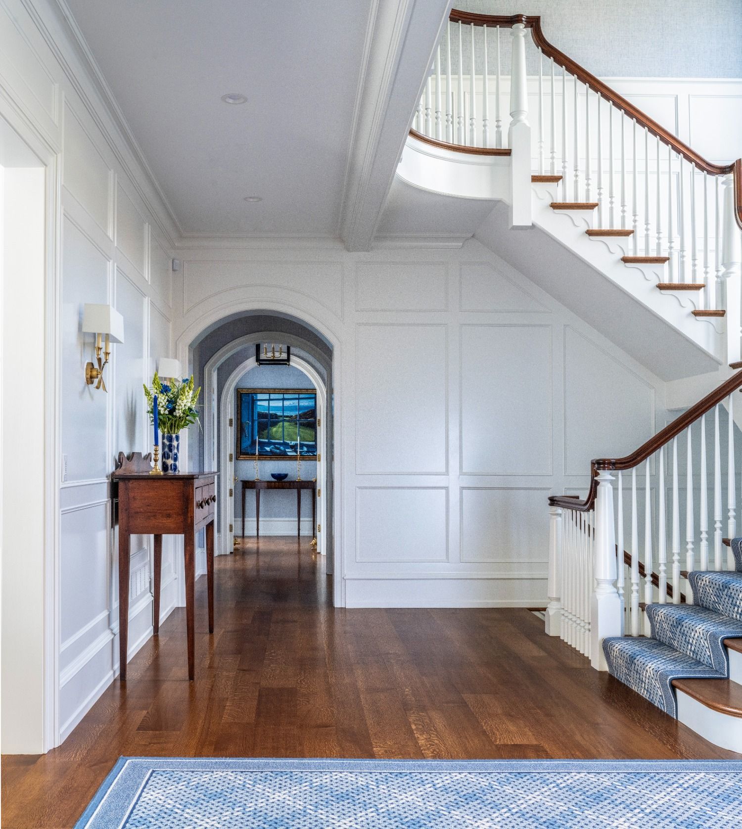A hallway with a staircase and a blue rug