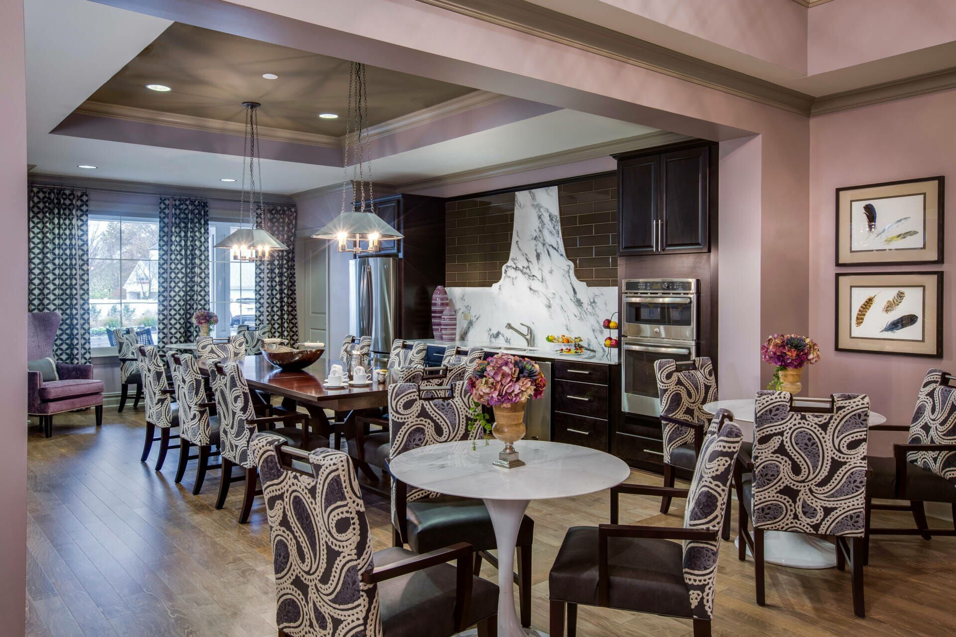 A dining room with tables and chairs and a kitchen in the background.