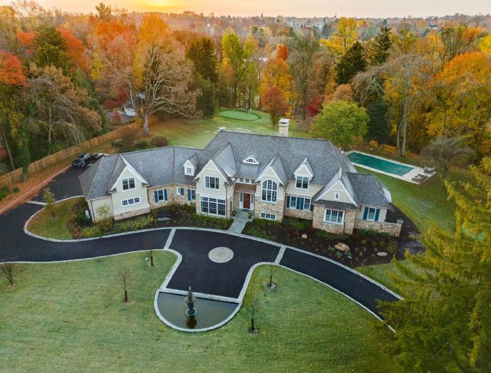 Aerial view of a large, luxurious home with a long winding driveway surrounded by vibrant autumn trees and a swimming pool.