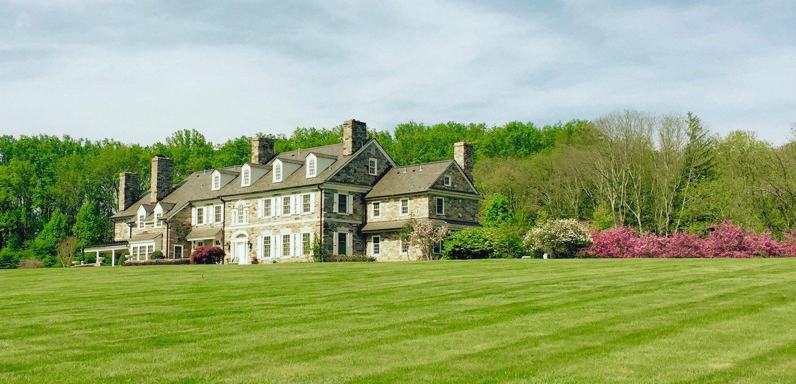 A large house is sitting in the middle of a lush green field.