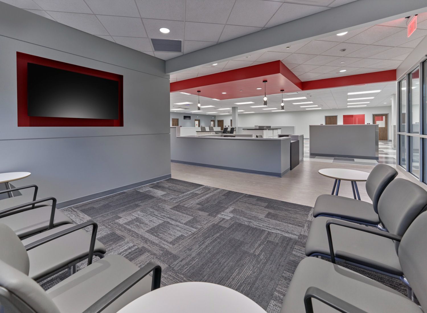 A waiting room with chairs , tables and a flat screen tv on the wall.