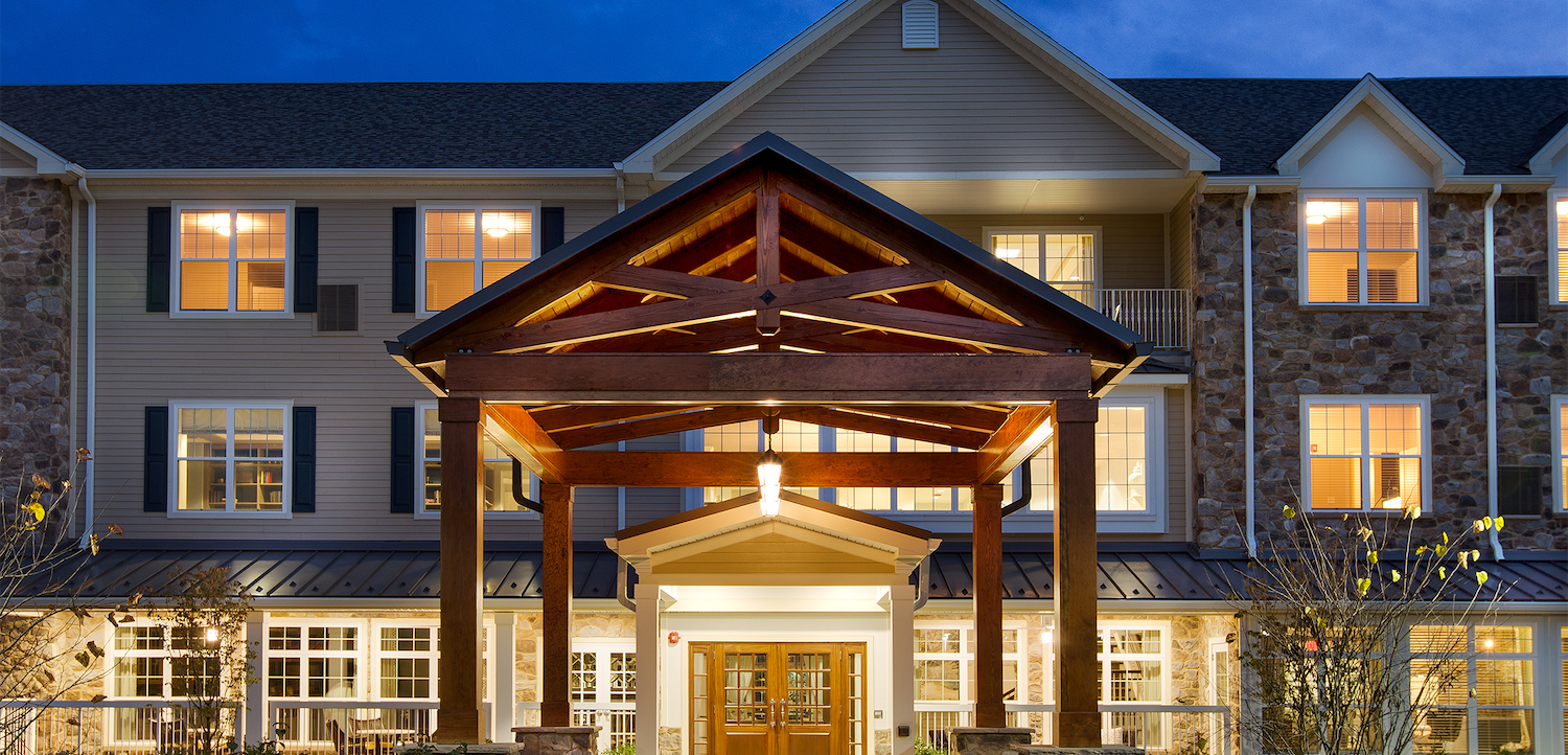 A large building with a wooden porch and a lot of windows is lit up at night.