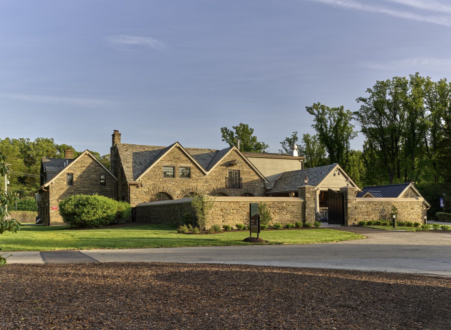 A large stone house sits on the side of a road surrounded by trees.