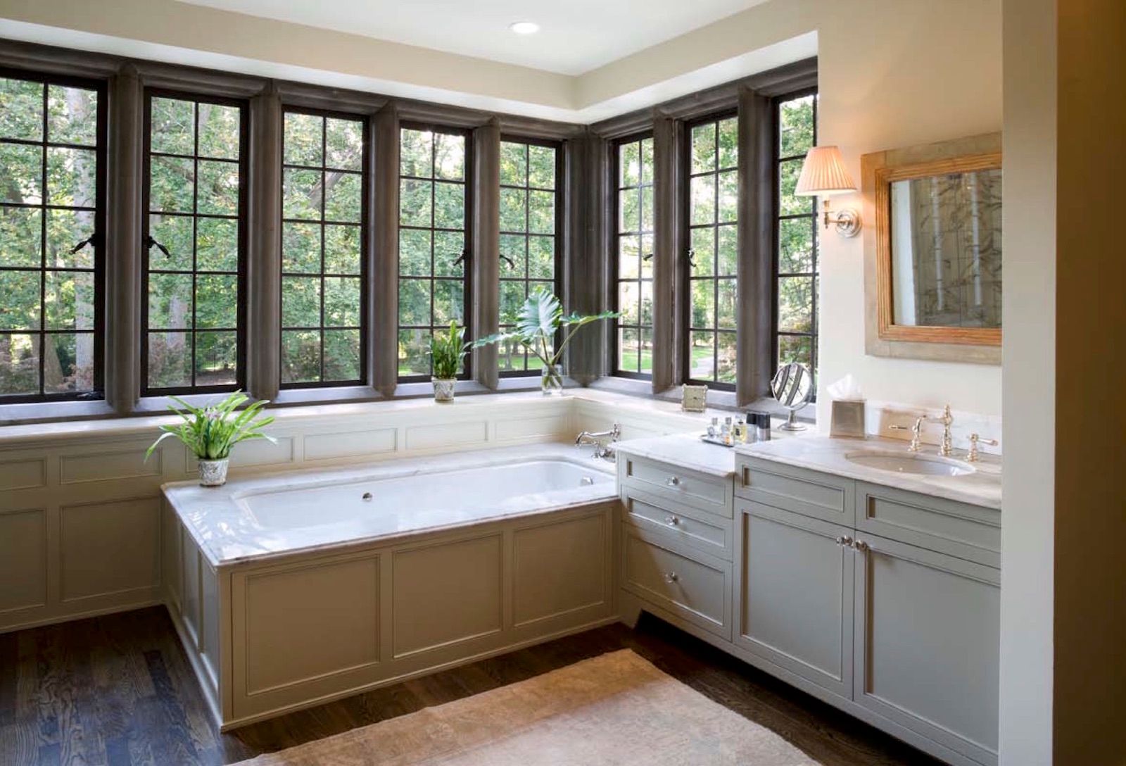 A bathroom with a bathtub , sink , mirror and lots of windows.