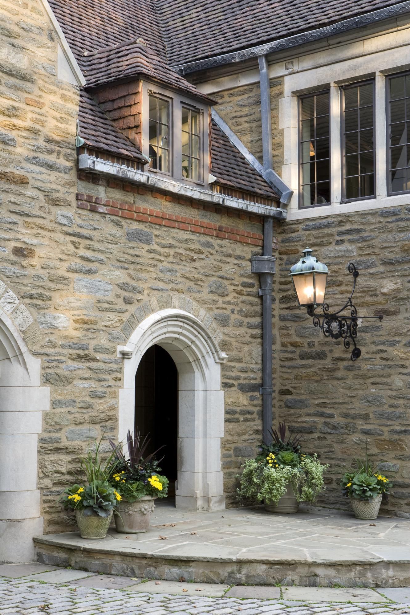 A stone building with a lantern and potted plants in front of it.