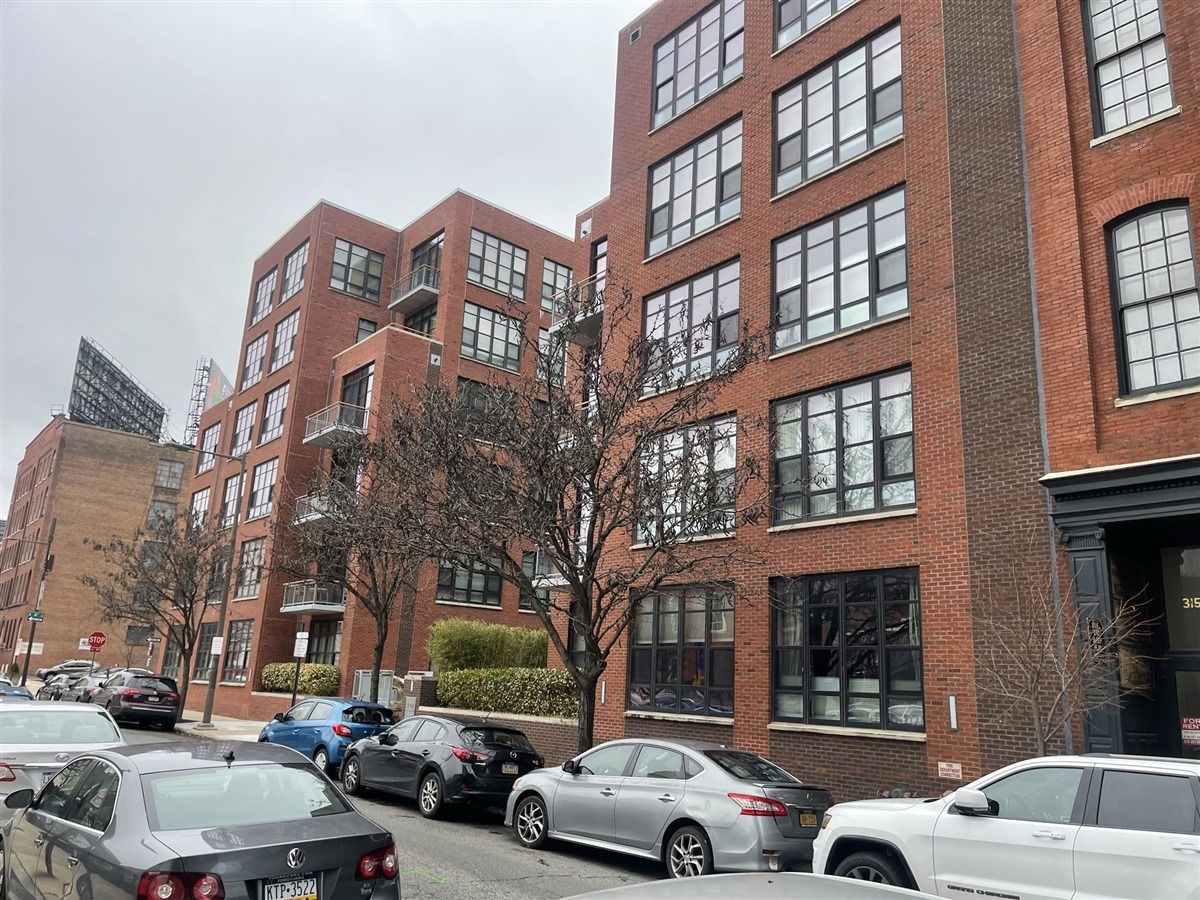 A row of cars are parked in front of a large brick building.
