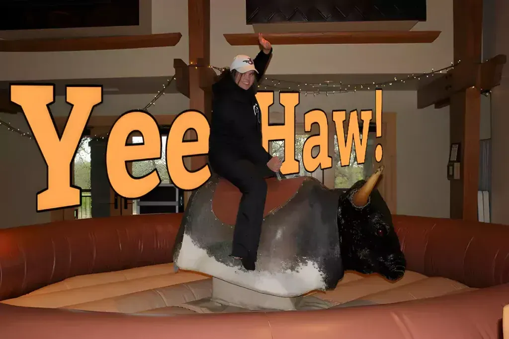 A man is riding a mechanical bull with the words yee haw behind him.