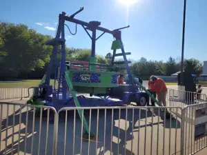 A group of people are working on a carnival ride behind a fence.