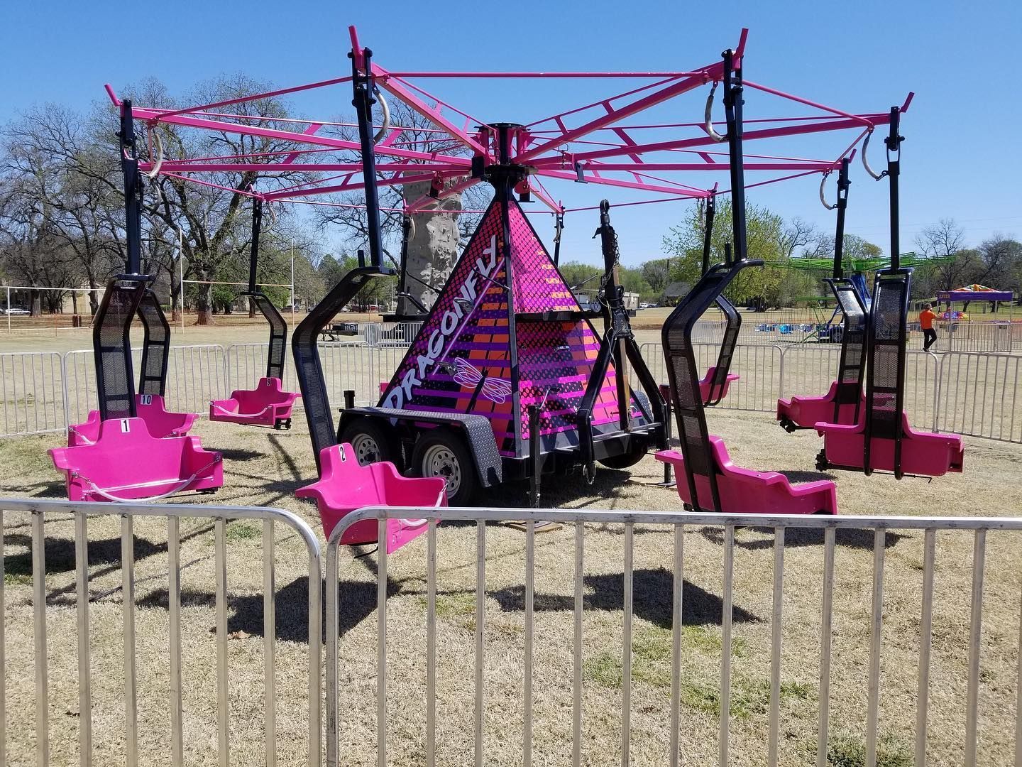 A pink carnival ride is behind a fence in a field.