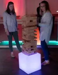 Two women are standing next to a stack of wooden blocks.