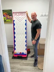 A man is standing next to a blinko game in a room.