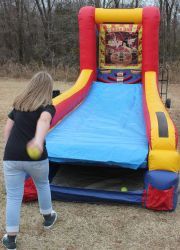 A young girl is throwing a tennis ball at a bouncy house.
