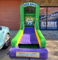 A green and purple inflatable bowling alley is parked in front of a building.