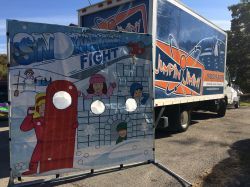 A truck is parked in a parking lot next to a painting of a snowman.