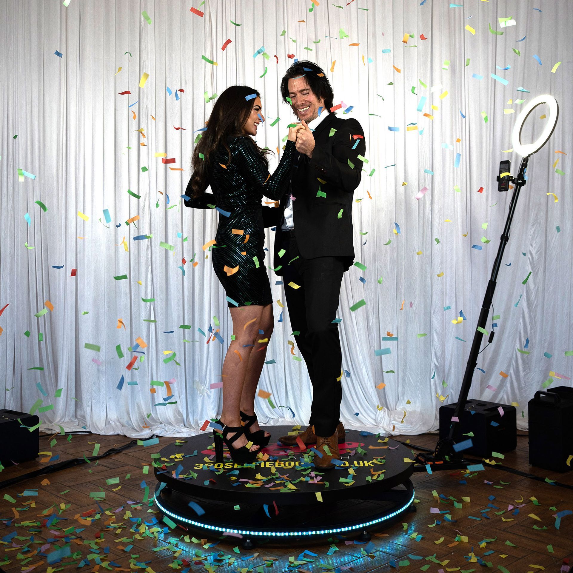 A man and a woman are standing on a turntable or the 360 photo booth
