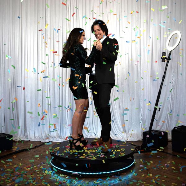 A man and a woman are standing on a turntable or the 360 photo booth