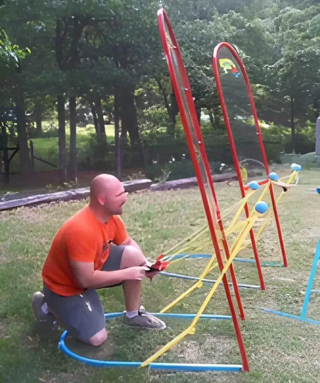 A man in an orange shirt is kneeling down in the grass