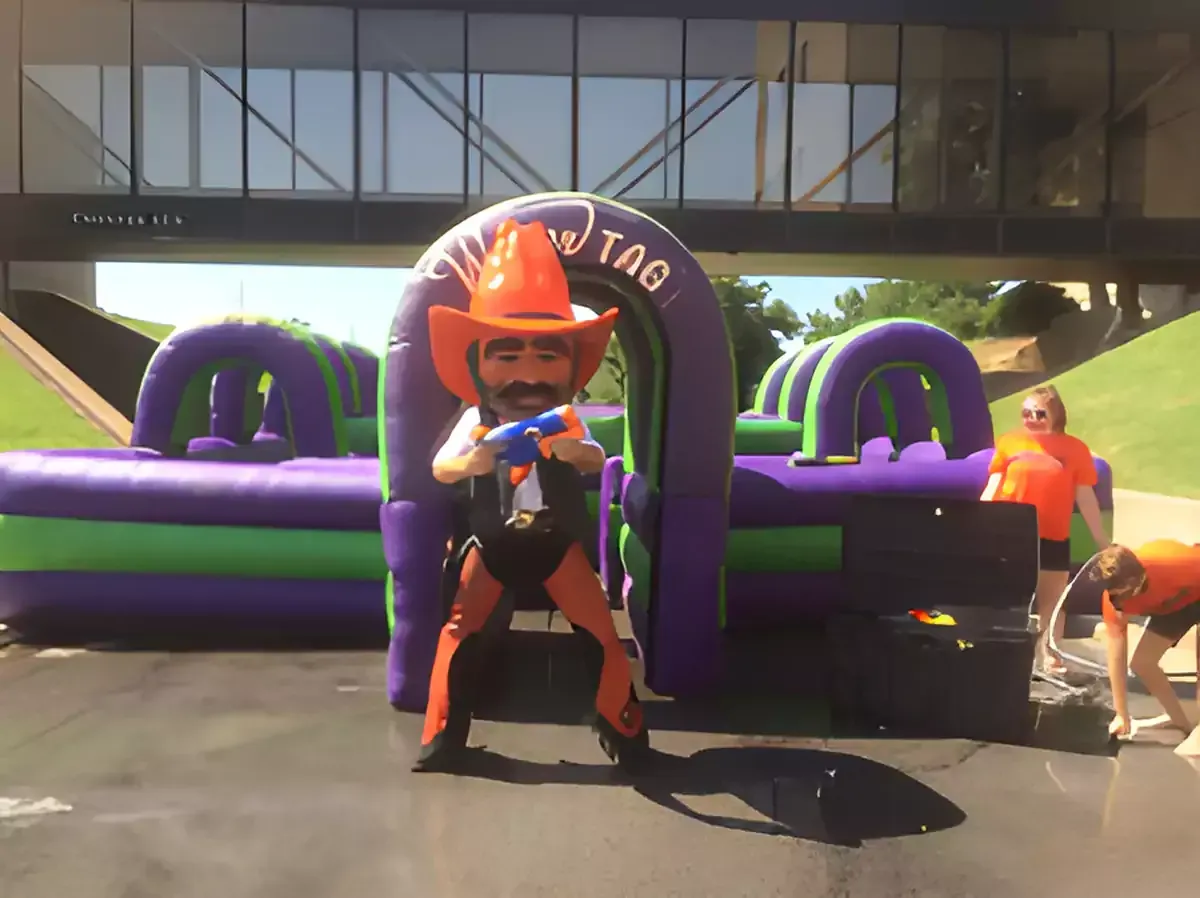 A man in a cowboy outfit is standing in front of an inflatable obstacle course.