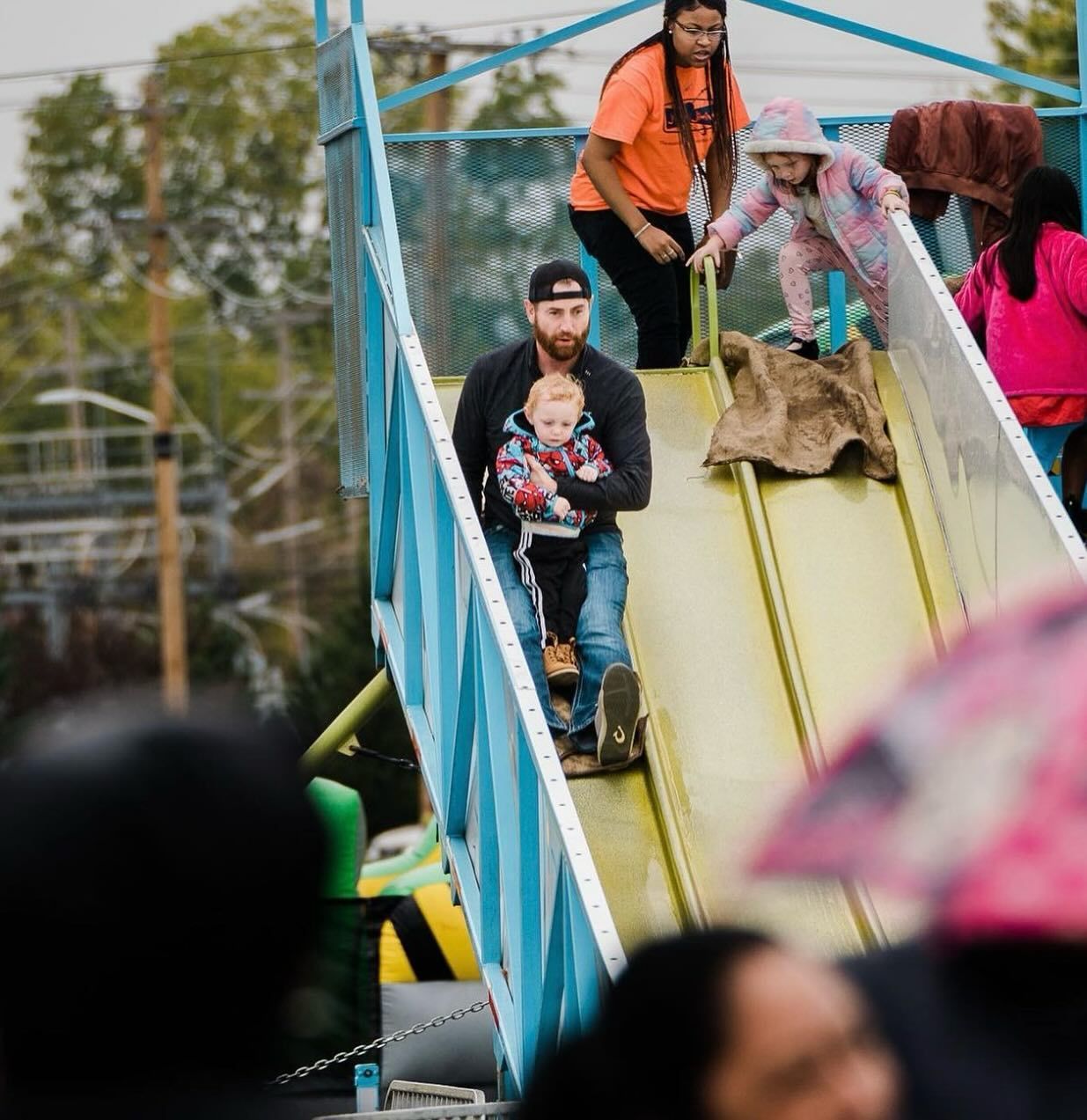 A man is carrying a baby down a slide at a carnival