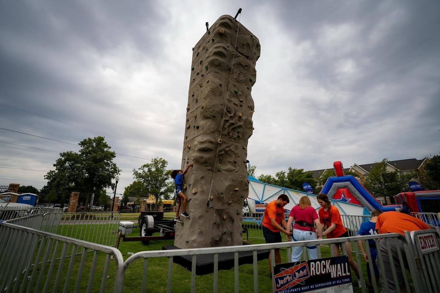 A group of people are standing around a climbing wall in a park.