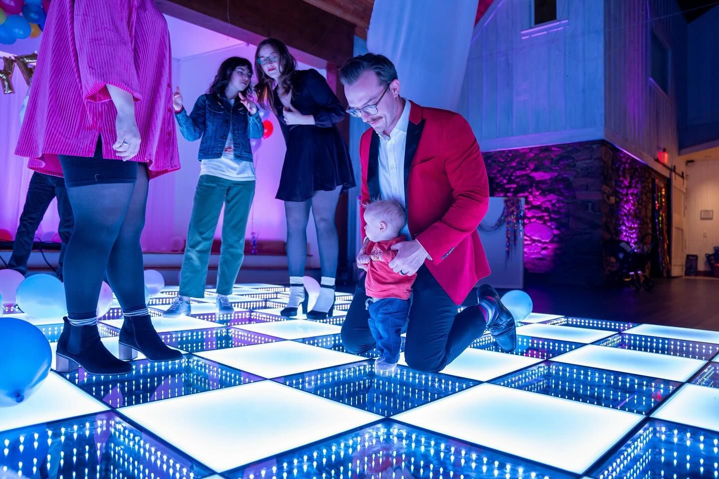 A man is kneeling down with a baby on a dance floor.
