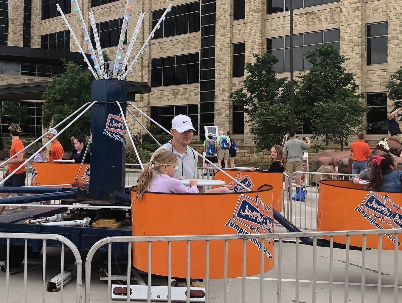 A man and a little girl are riding a carnival ride behind a fence.