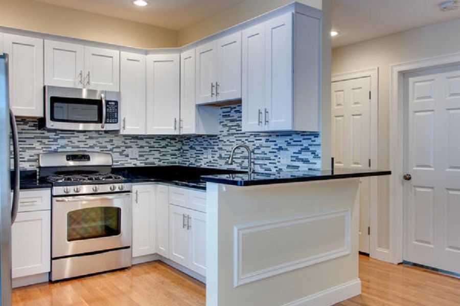 White kitchen with stainless steel appliances, black countertops, and mosaic tile backsplash.