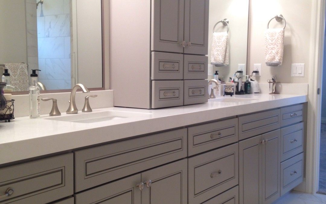 Gray bathroom vanity with overhead cabinets, white countertop, and silver fixtures.