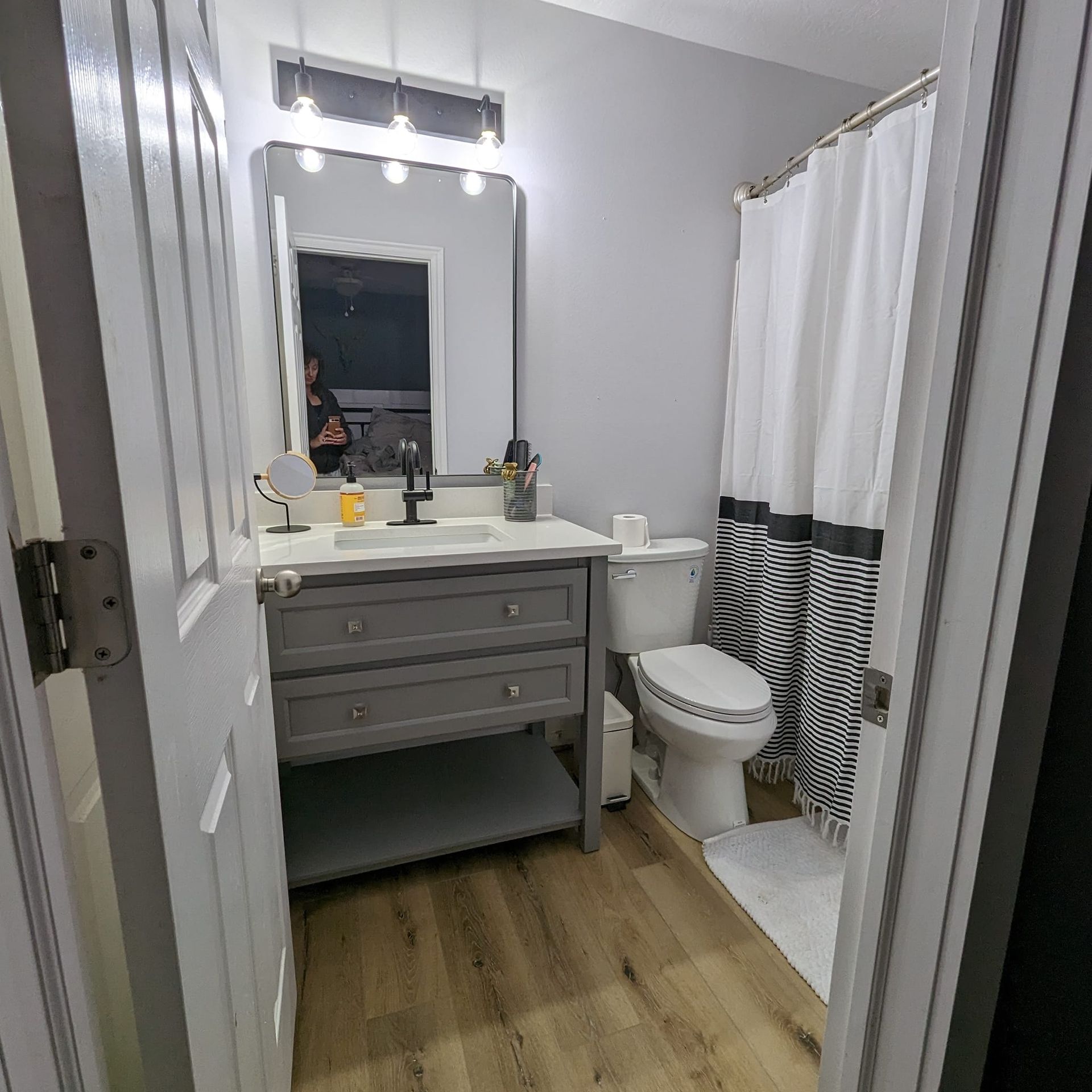 Bathroom interior with gray vanity, white toilet, and shower with black and white striped curtain.