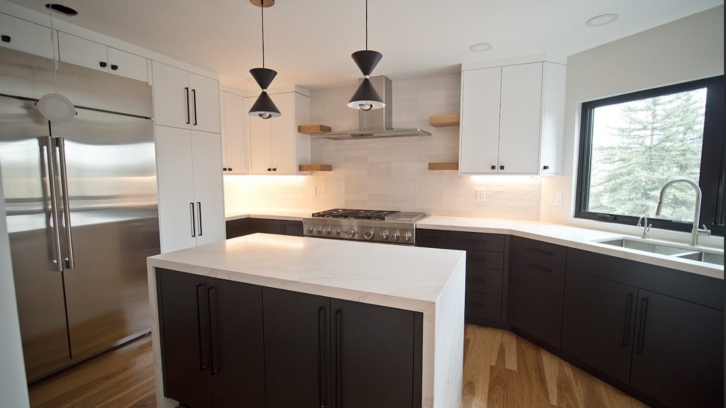 Modern kitchen with white countertops, dark cabinetry, stainless steel appliances, and pendant lighting.