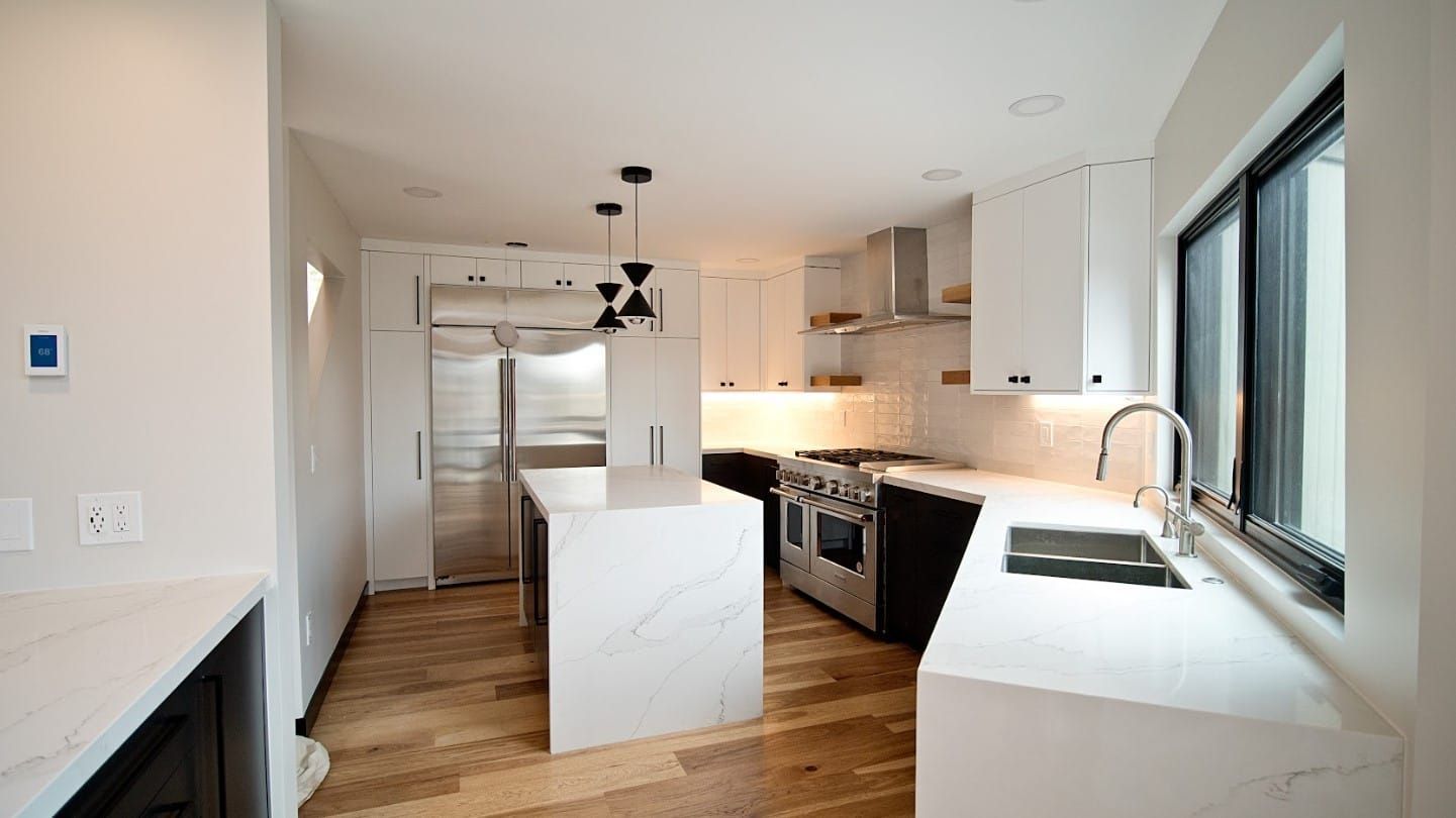 Modern white kitchen with stainless steel appliances, marble countertops, and light wood flooring.