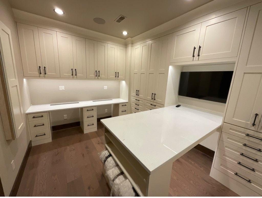 Home office with white cabinets, desk, and TV. Brown wood floor.