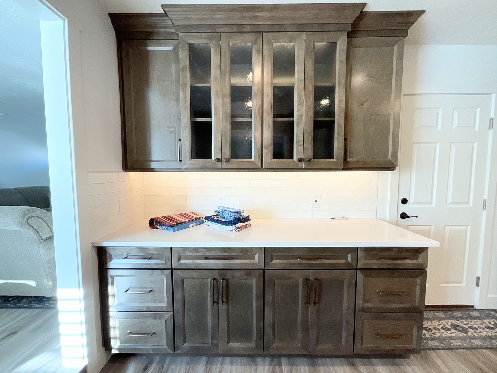 Gray cabinetry with white countertop, white backsplash, and glass-front upper cabinets.