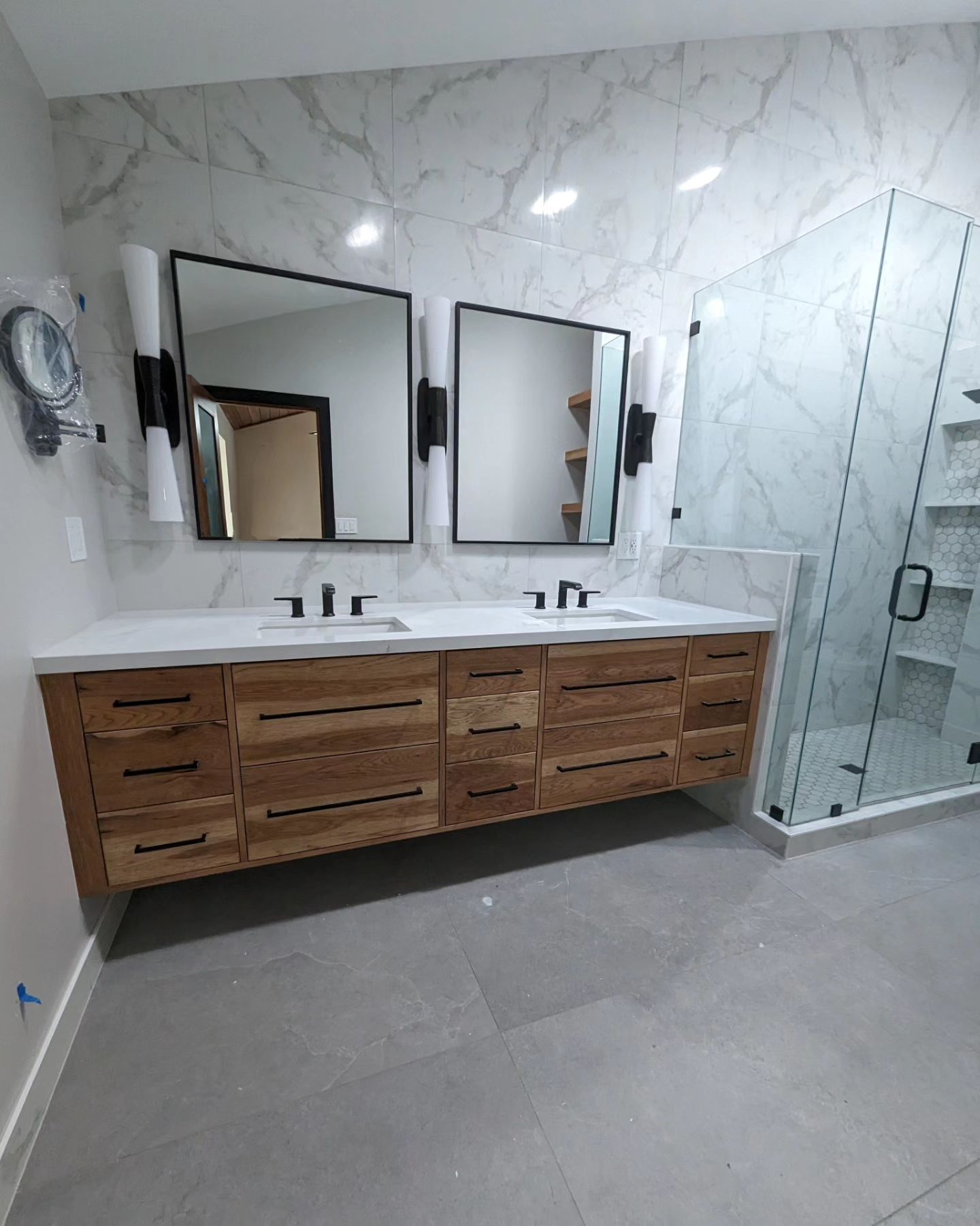 Modern bathroom with wooden double vanity, marble wall, black mirrors, and glass shower.