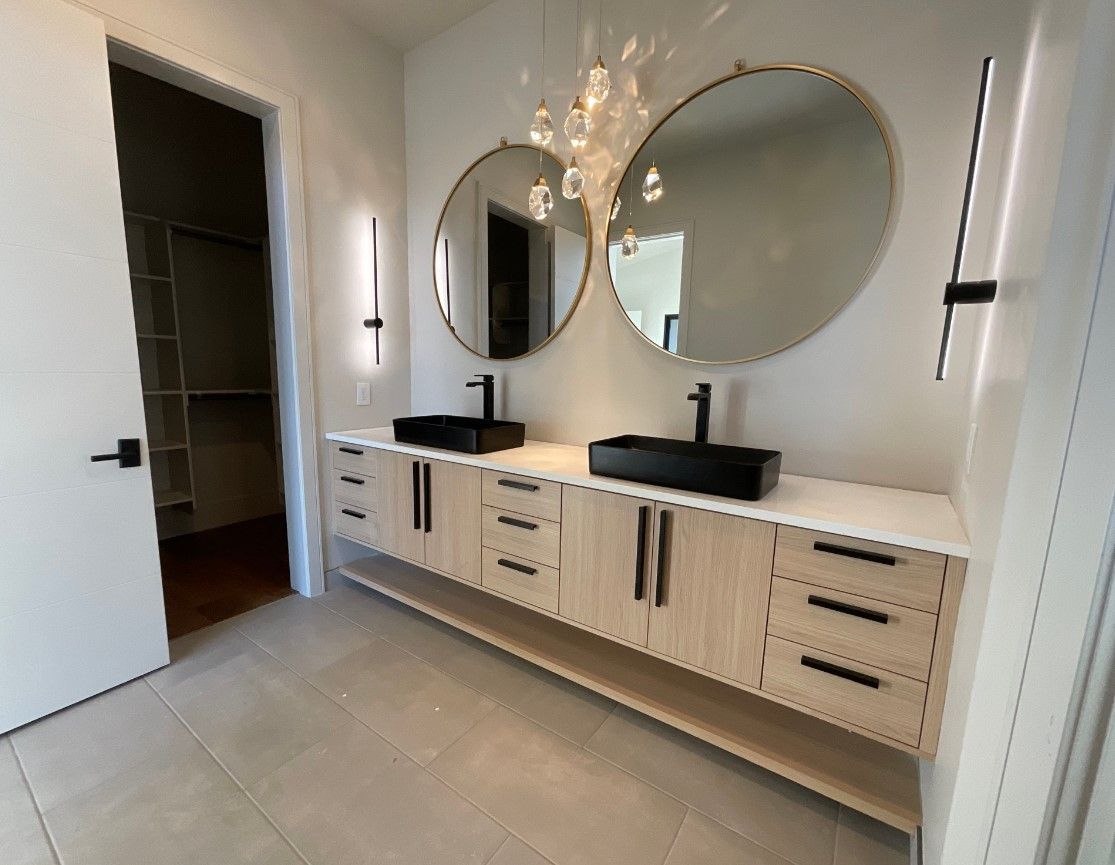 Bathroom with double vanity, two round mirrors, black sinks, and a closet.
