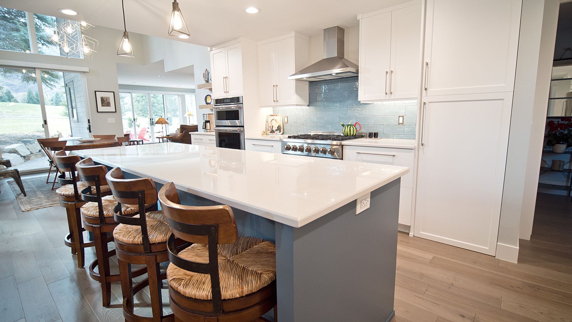 Modern kitchen with white cabinets, island, wooden floor, and bar stools.