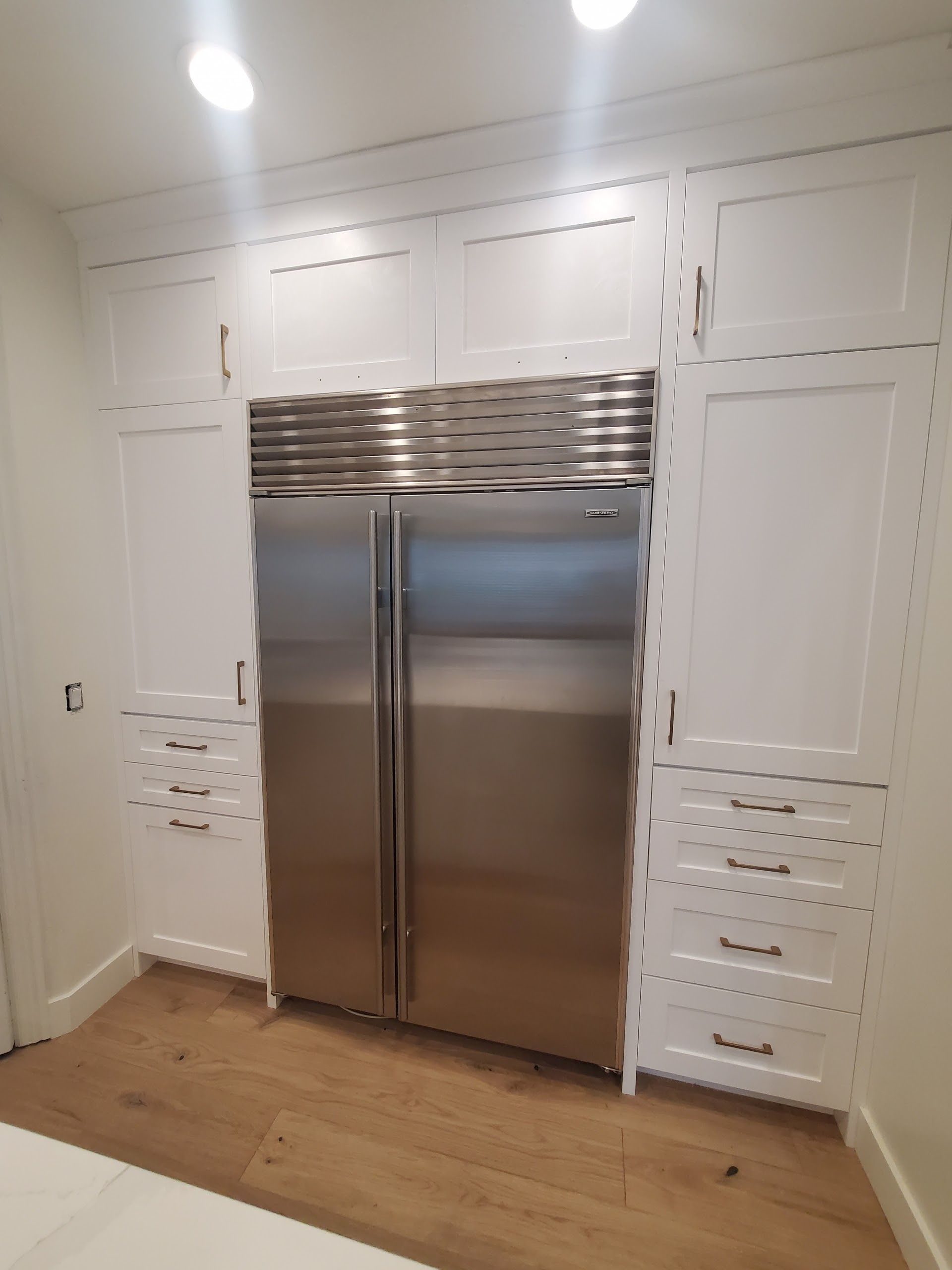 Stainless steel refrigerator built into white kitchen cabinets.