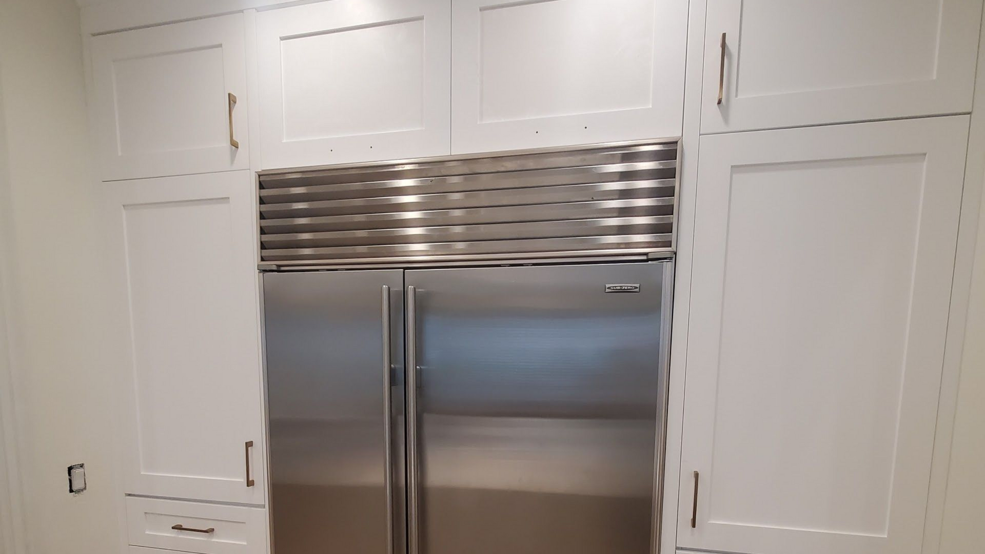 Stainless steel refrigerator built into white cabinetry in a kitchen.