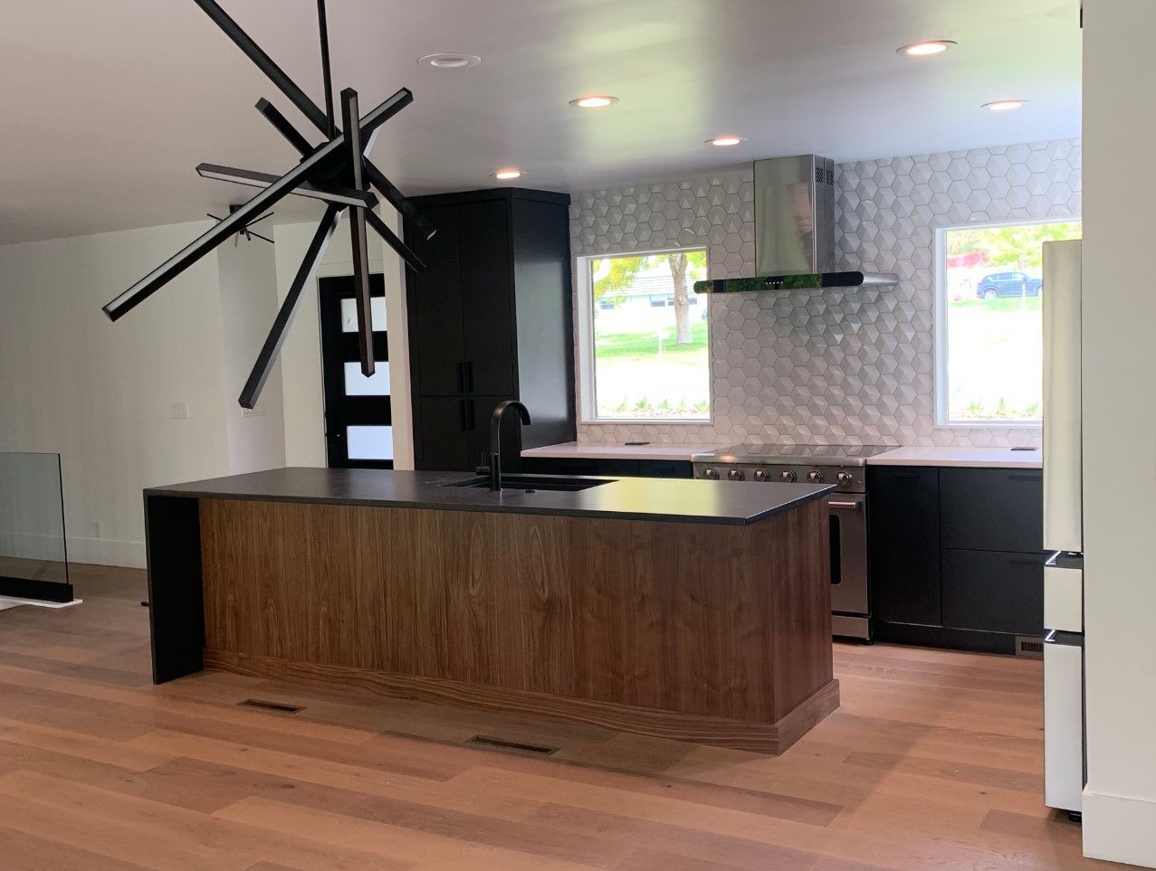 Modern kitchen with wood island, black cabinets, white backsplash, and a unique chandelier.