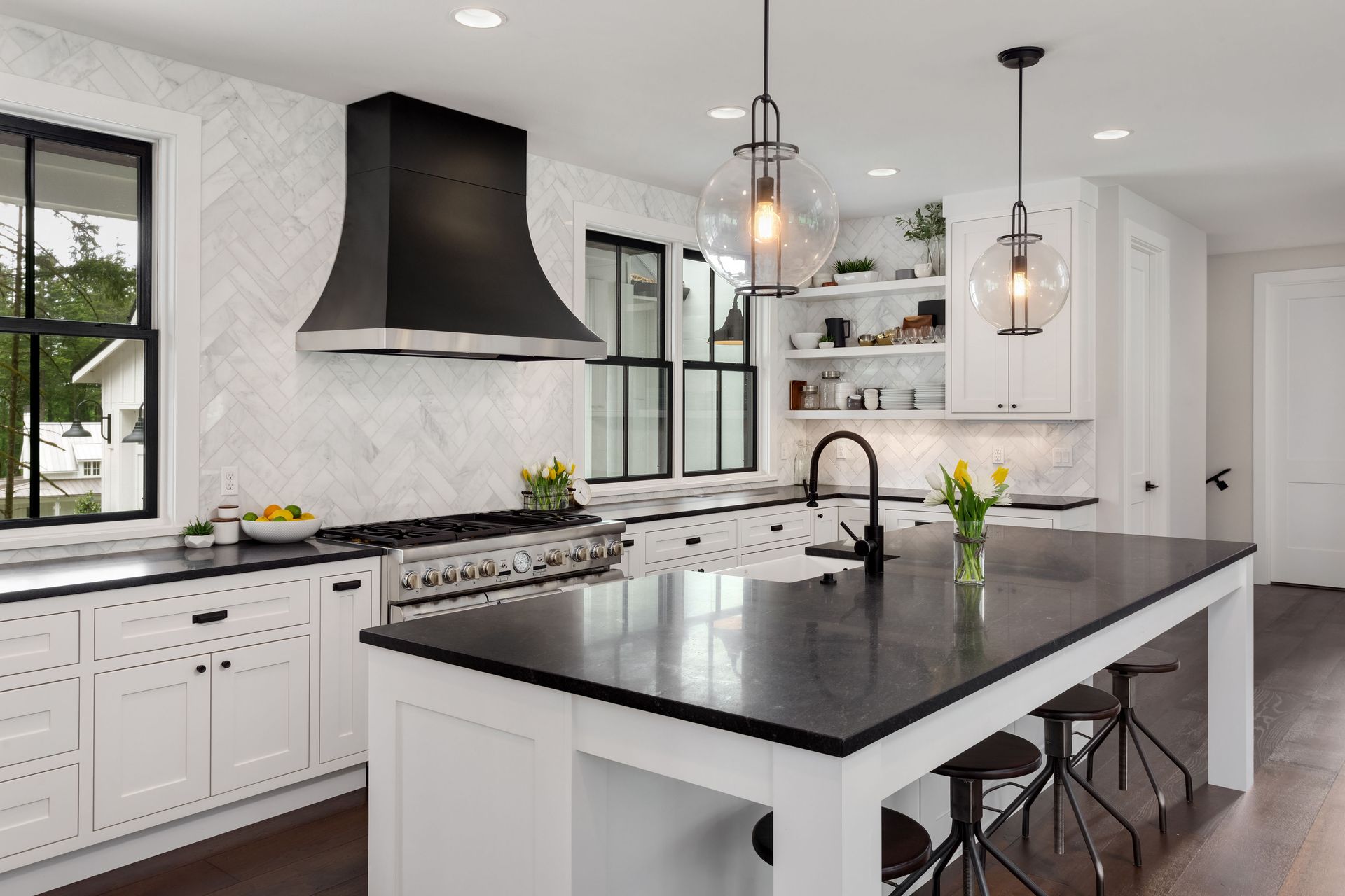 Modern white kitchen with black accents; island, range hood, and windows.