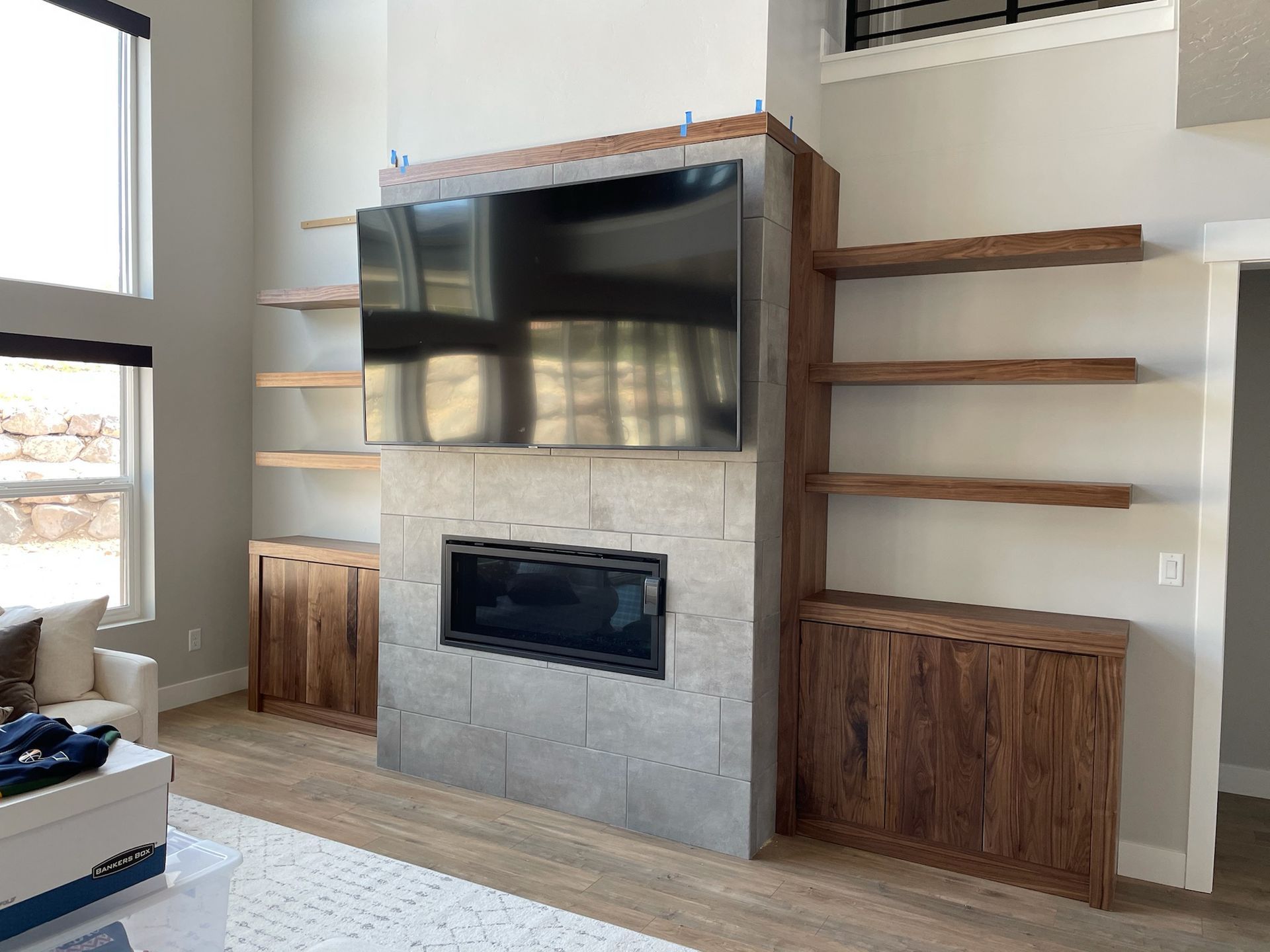 Living room with fireplace, TV, built-in shelves and cabinets. Light gray stone surround and wood elements.