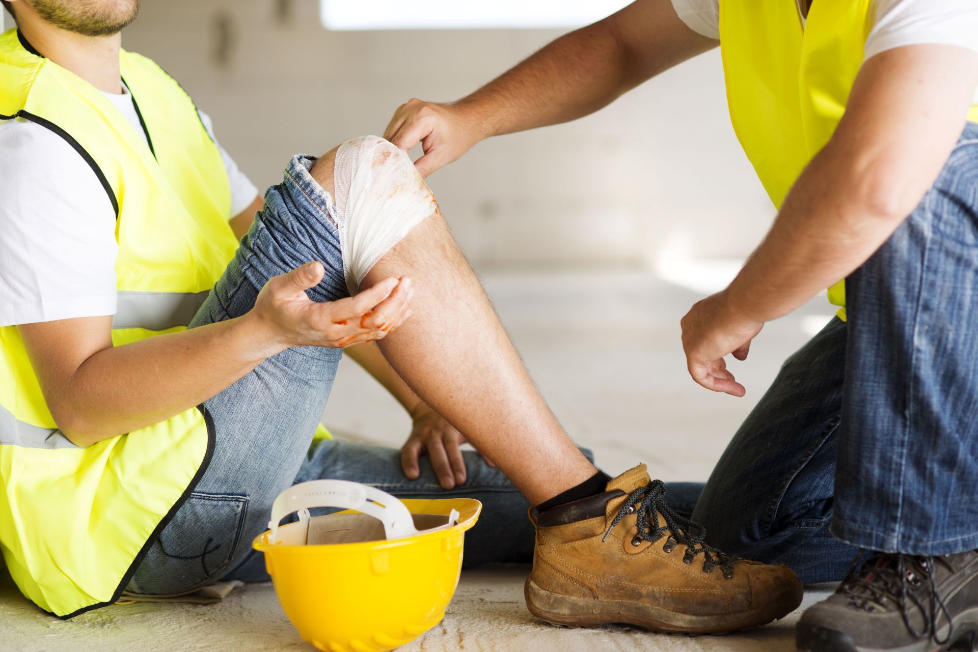 A construction worker is sitting on the floor with a bandage on his knee.