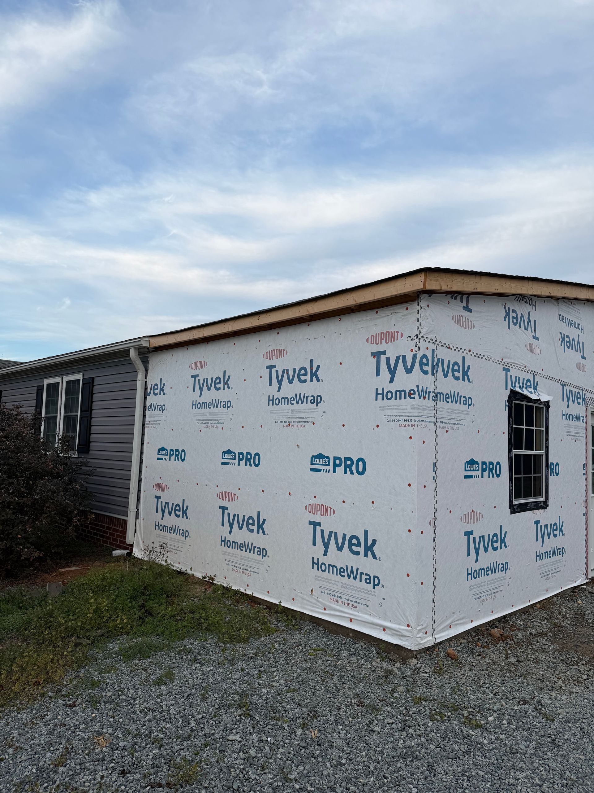 A mobile home exterior undergoing construction with Tyvek house wrap installed over the side walls.