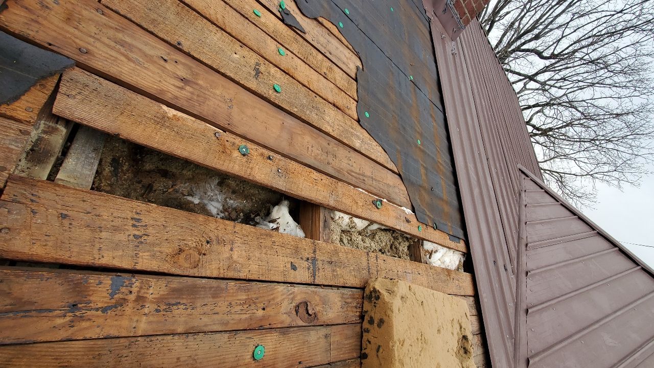 A close-up view of a damaged roof with missing shingles, exposed wood slats, and insulation underneath.