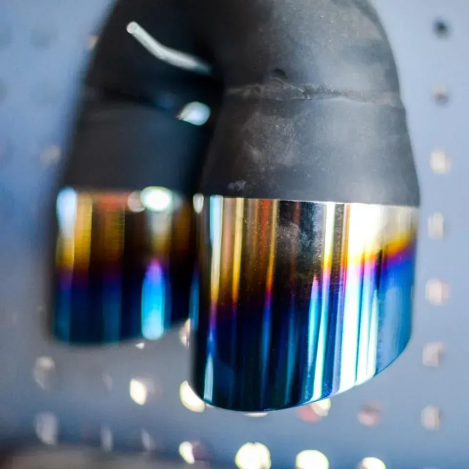 Pair of iridescent exhaust tips with a black bend, mounted on a perforated surface.