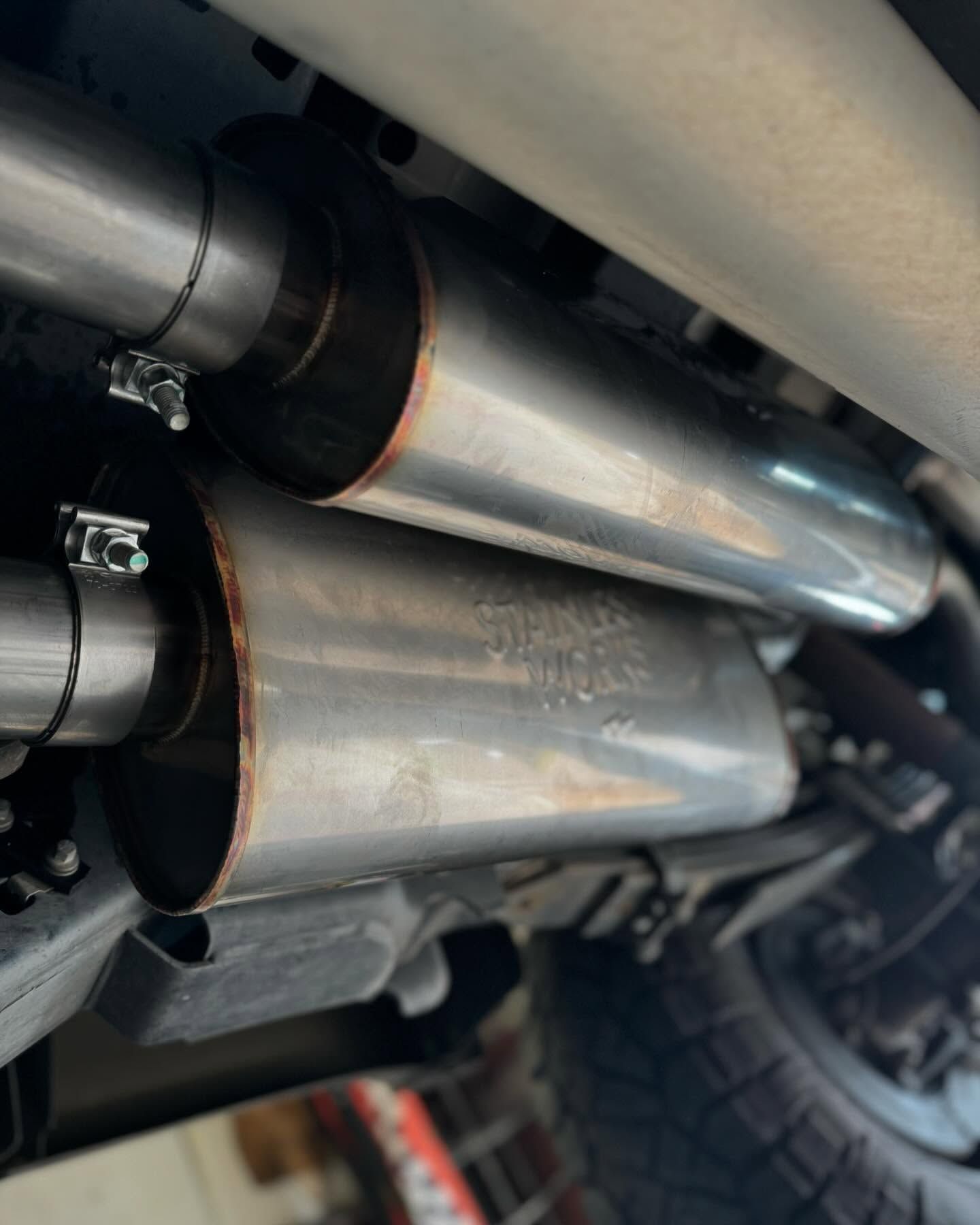 Two shiny chrome exhaust mufflers installed under a vehicle, held by clamps.