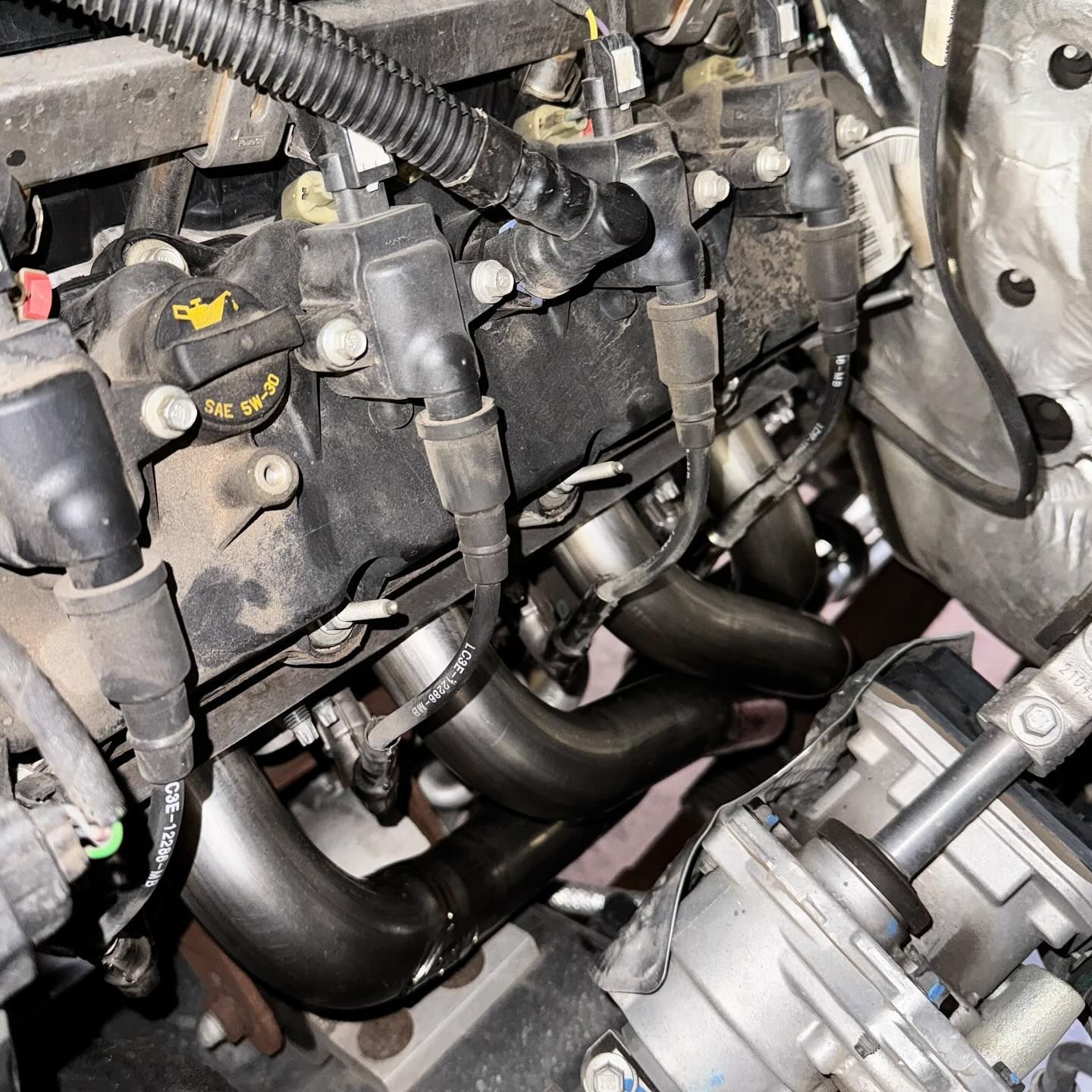 Close-up of a car engine with black exhaust headers and spark plug wires visible.