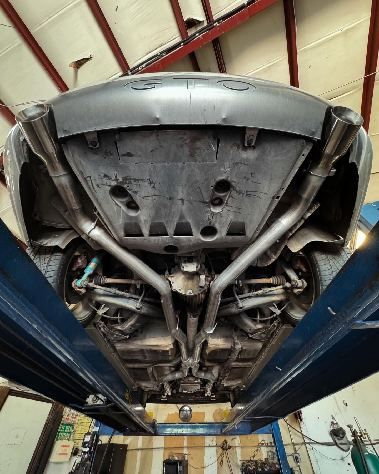 Undercarriage of a gray car on a lift, showing custom exhaust system and suspension components.