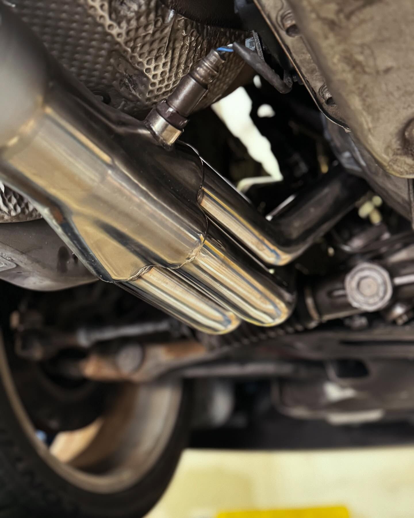 Undercarriage view: shiny exhaust pipes near a car wheel and mechanical components.