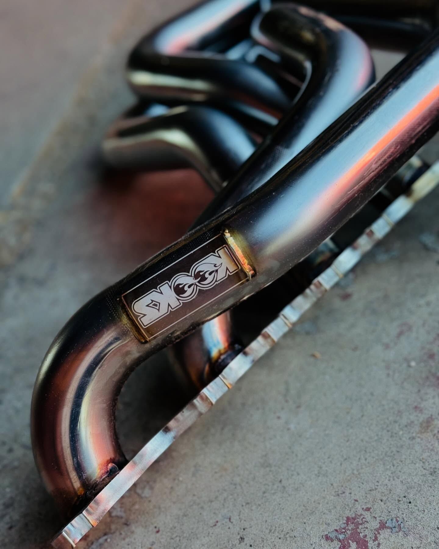 Shiny steel exhaust manifold on a concrete surface, showcasing welded construction.